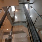 View of Glass Hoistway and Acrylic Elevator from lower landing to third floor showing main guide rail of cable inclinator down elevator