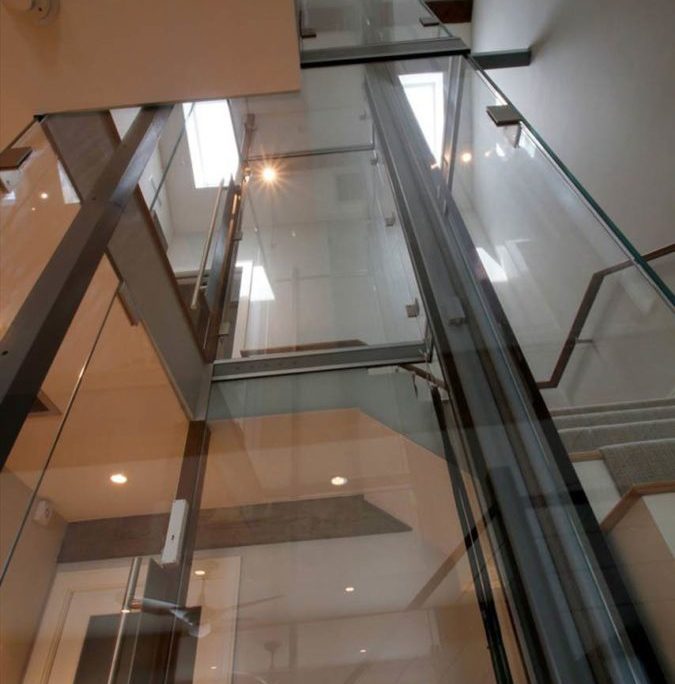 View of Glass Hoistway and Acrylic Elevator from lower landing to third floor showing main guide rail of cable inclinator down elevator
