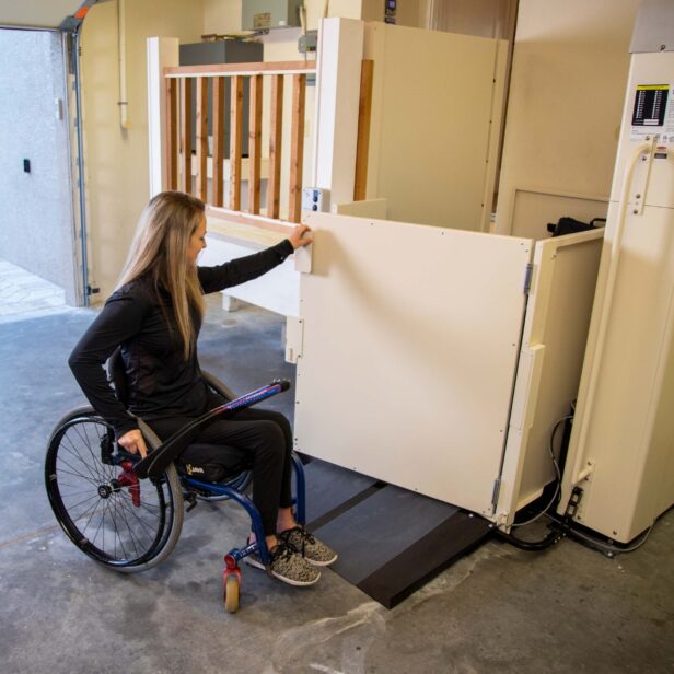 Woman in wheelchair is opening a powered lift door.